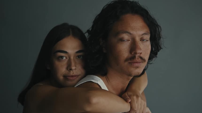 Portrait of a couple with the woman hugging the man from behind and both looking directly at the camera