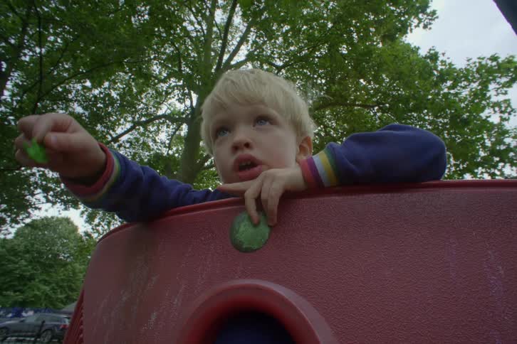 A blonde hair child with one arm stretched forward talking at the playground