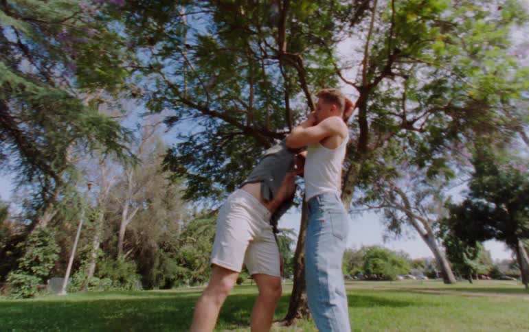 Two men dancing with physical contact in an outdoor environment with trees and grass