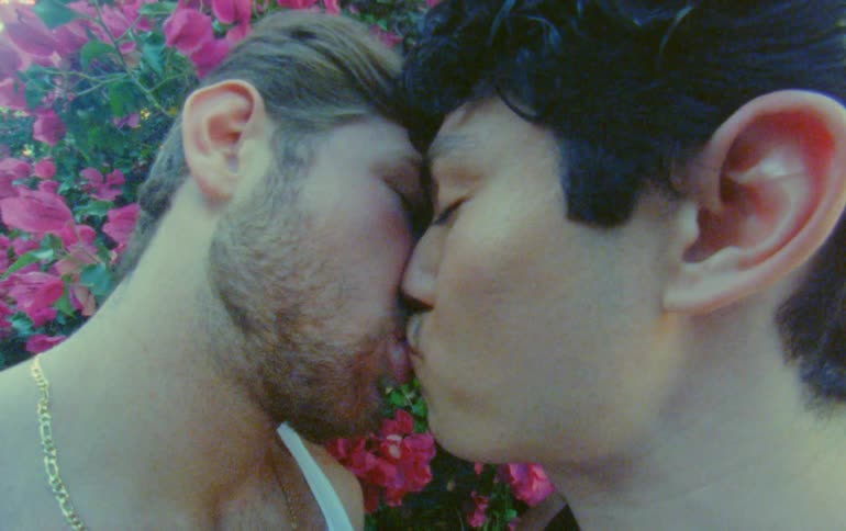 Close up of two men kissing and cuddling outdoors near flowering plants