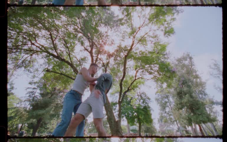 Two dancers dance in a park surrounded by tall trees