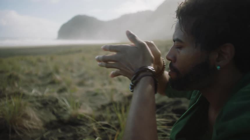 Man sitting on grass a distance from coast performs ritual to experience nature
