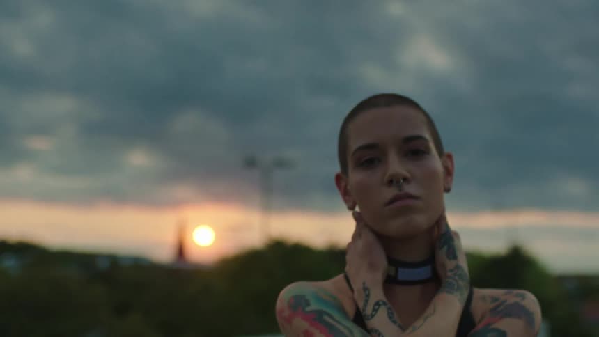 A woman with shaved hair and all tattoos places her two hands on his neck