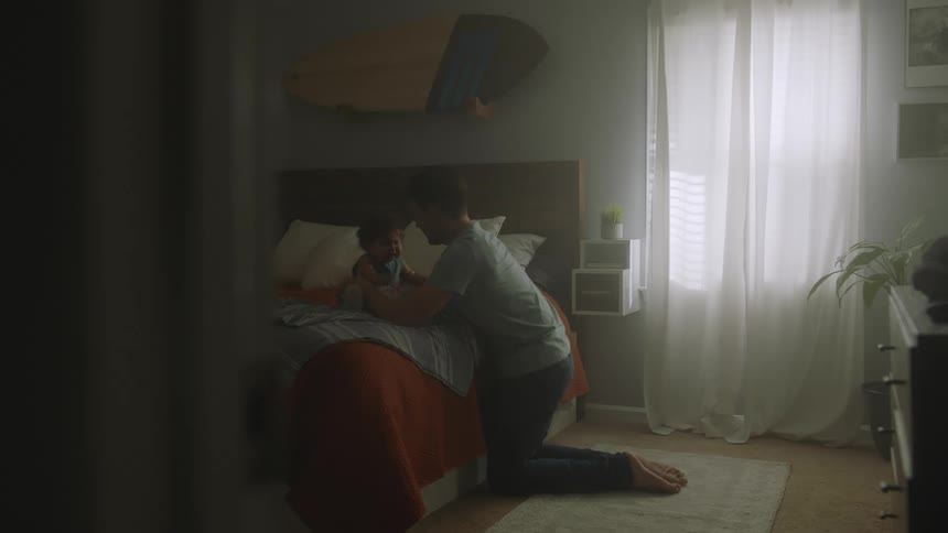 Man kneels on floor near bed and plays with baby