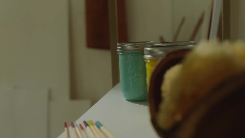 A person moving some jar of paint with different color from one table to a shelf