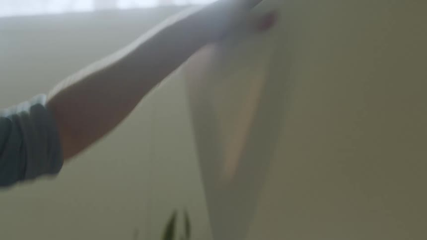 A man moving an art easel around a room in the middle of the day before putting a blank canvas on it