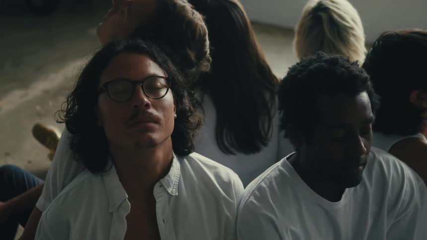A diverse group of young people are disconnected from reality as they sit motionless in a softly lit studio