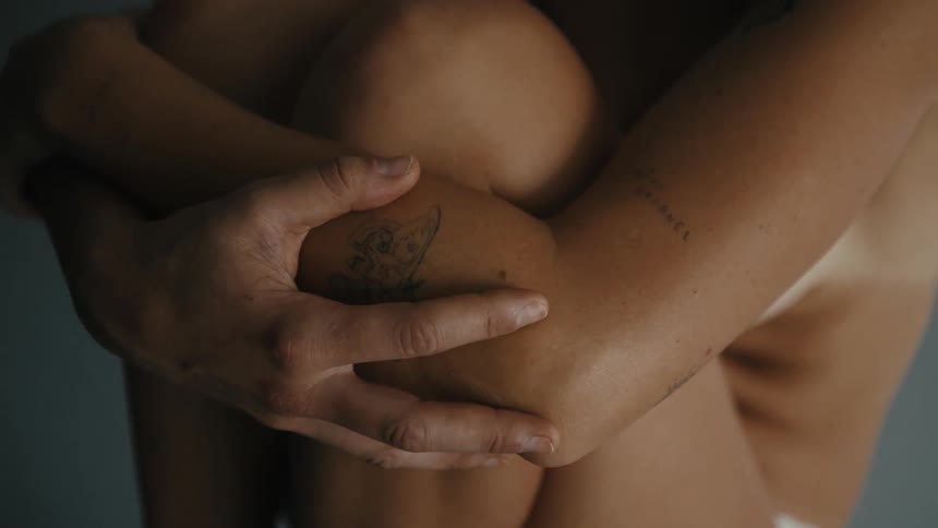 A female with tattoos holds her arms and legs close