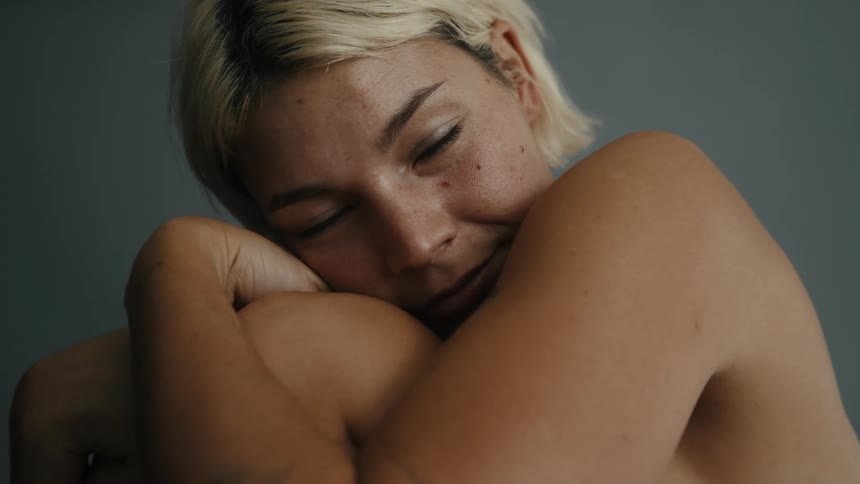 Blonde woman with her arms around her knees smiles slightly