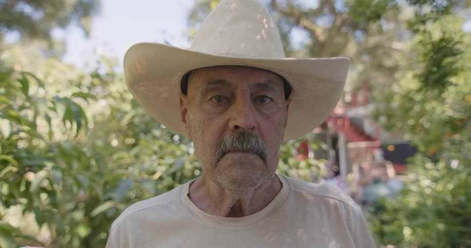 An old man wearing a cowboy hat on a sunny day