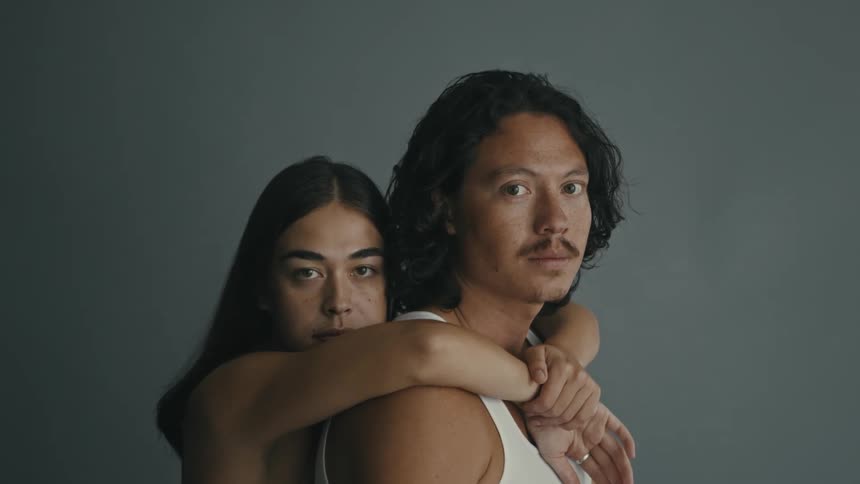 A couple embraces, and holds the camera in a gaze