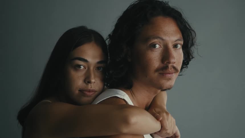 Close up of a woman hugging a man from behind around his shoulders as they both look the same direction