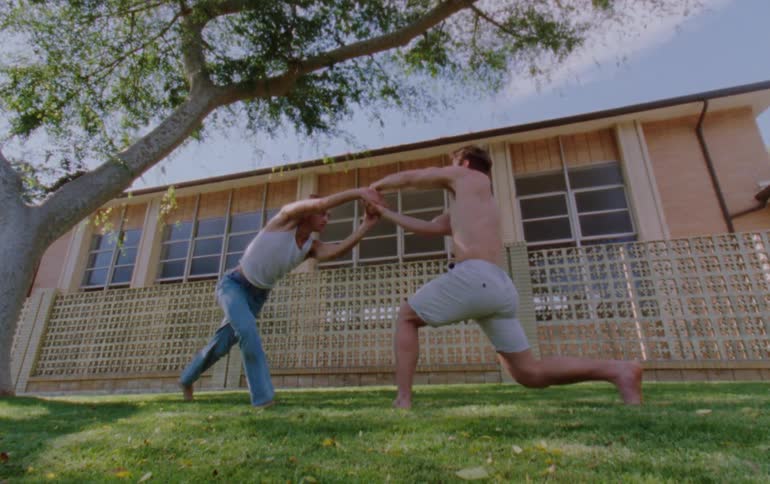Two men doing a dance together on a lawn in front of a building