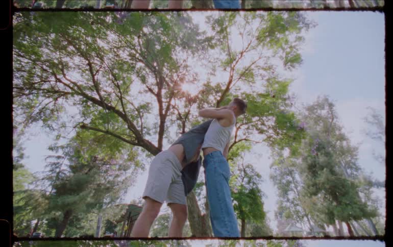 Two men dancing face to face with physical contact in an outdoor environment with trees and vegetation