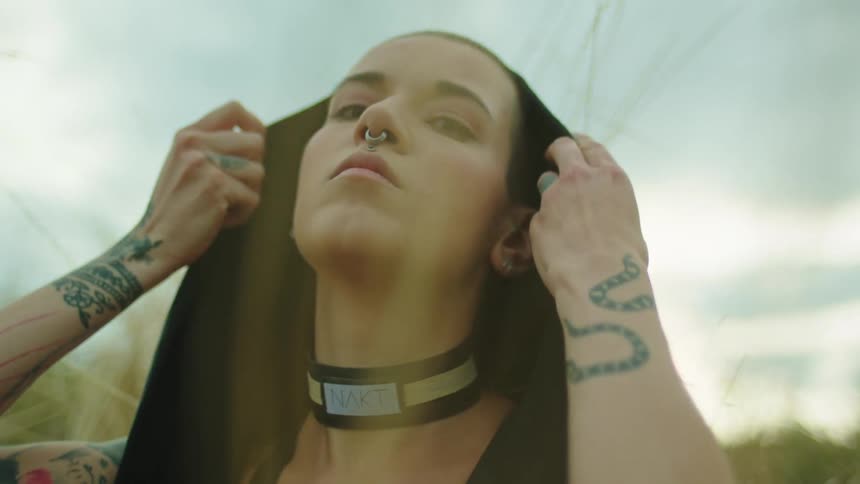 Young tattooed woman with nose ring puts on a hoodie in the countryside