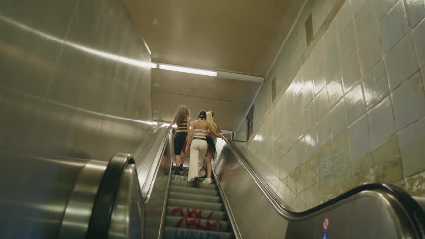 Three women ride up the subway escalator