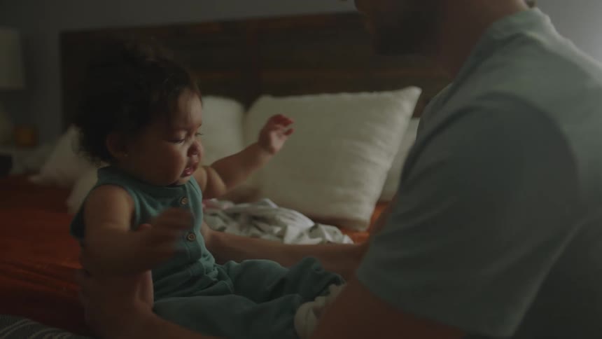 A man arranging his baby daughters clothes which is on top of a bed