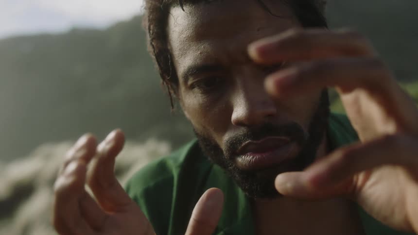 A black man with a beard wearing a green jacket using his hands in a circular way