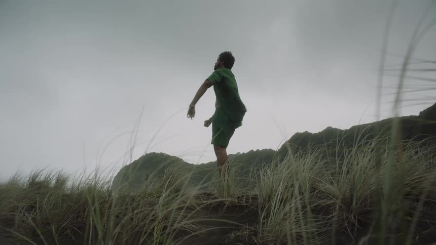 Man dancing gently in a natural location with vegetation and a breeze of wind