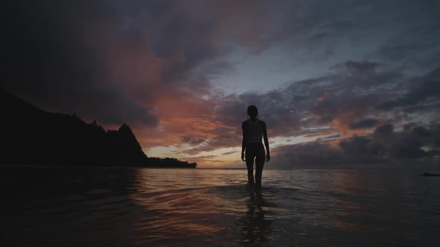 A woman walking along a dark beach with the sunset in the sky