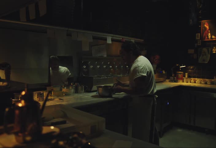 A man is preparing a pizza in a dimly lit kitchen