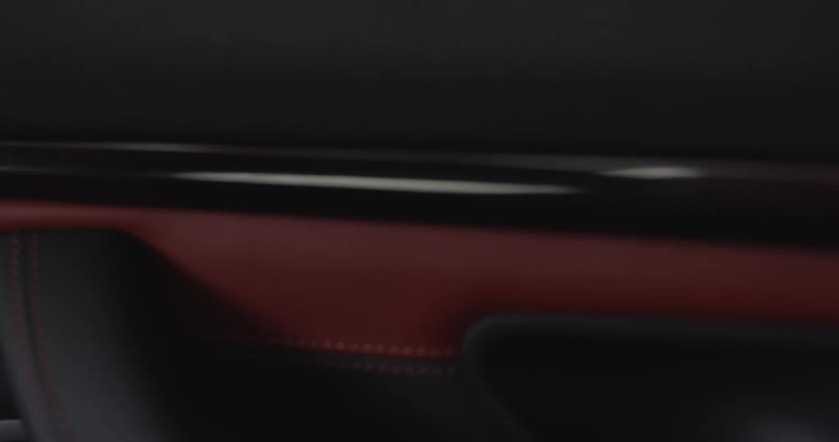An interior of a car door where there is a handle and stitched leather texture on the door frame