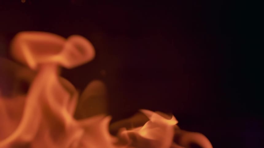 Close up of flames from a fire in a dark room as particles from the flame fly around
