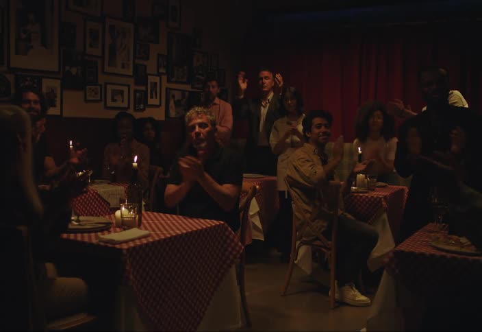 Men and women sitting at dining tables in a restaurant while listening intently and then standing up and clapping