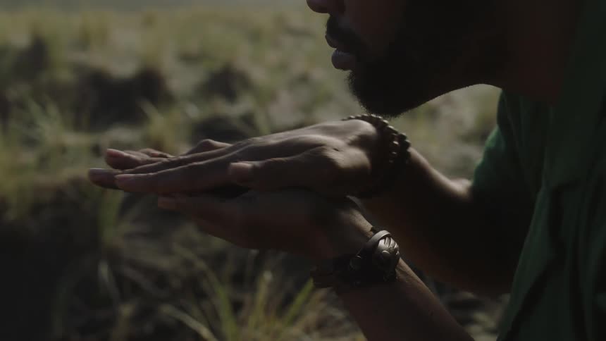 A man stands in a field of grass worshiping and making hand gestures with dirt
