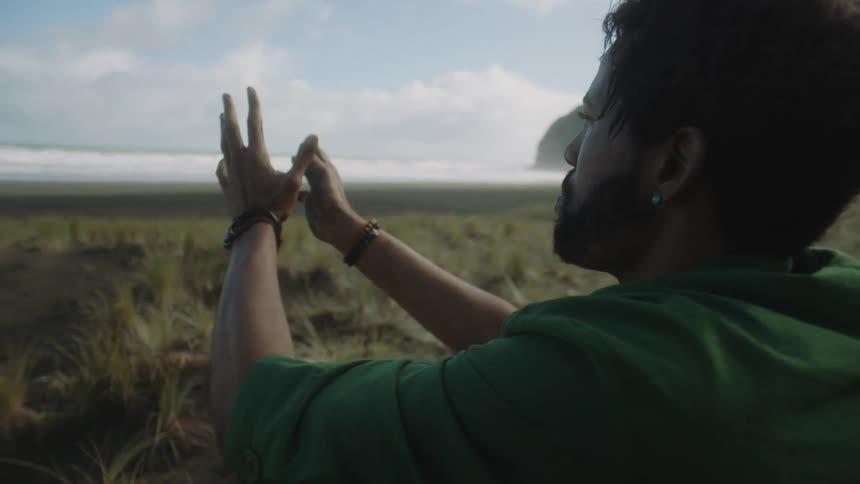 A man stands in the grass making worshiping hand gestures in front of him