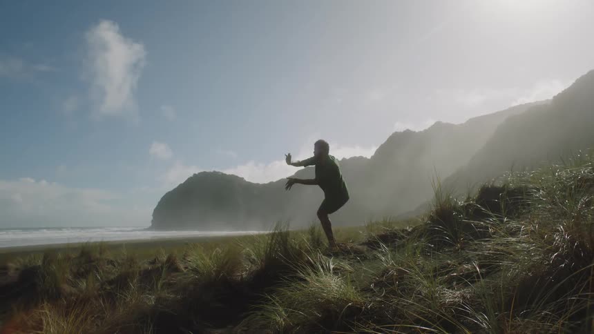 A man doing yoga moving his body on a beach with mountains in the background