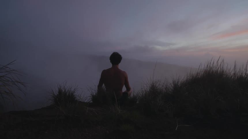 Man meditates on shore under red tinted clouds