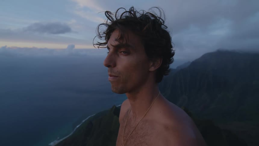 A man stands on the mountain peak and looks over the ocean