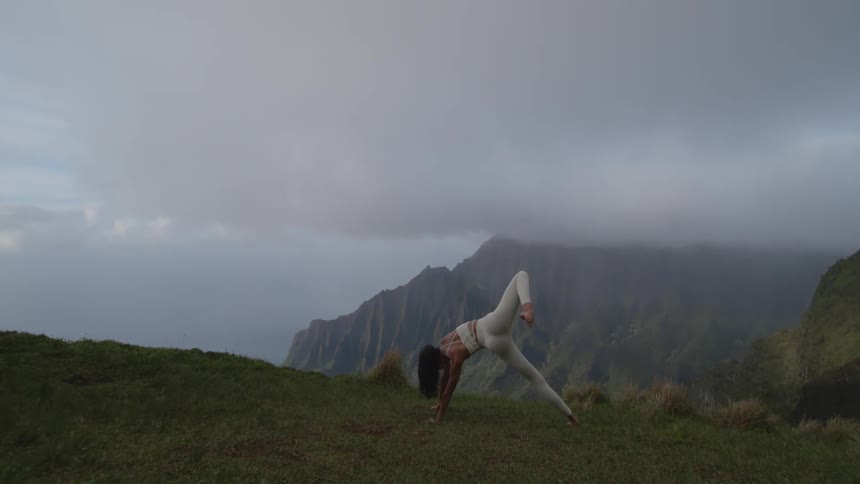 A woman doing yoga stretching her body in nature on a mountain edge overlooking fog covered mountain ranges