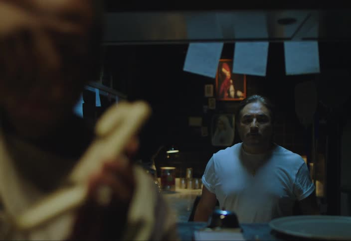 A man walks up to a phone and answers it writing something down on a piece of paper and then hands it to a man in a kitchen