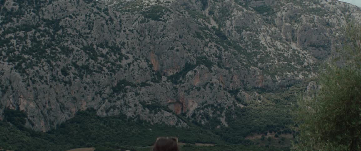 A woman with her baby strapped to her looks at a mountain