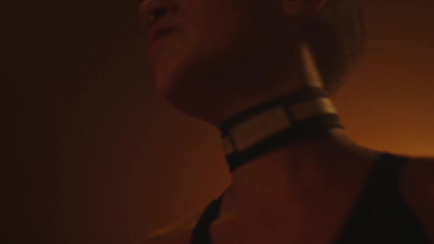 A bald woman with tattoos dances under dim lights