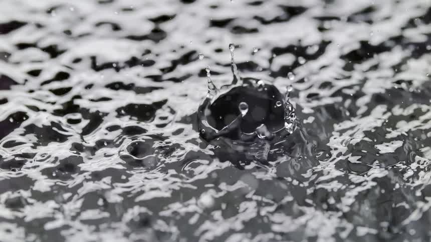 Close up of water droplets splashing on a water surface creating ripples and roughness on the water