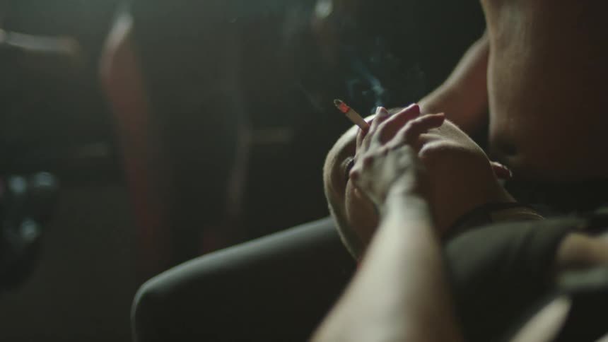 Close up of a woman smoking a cigarette while laying on a mans lap indoors