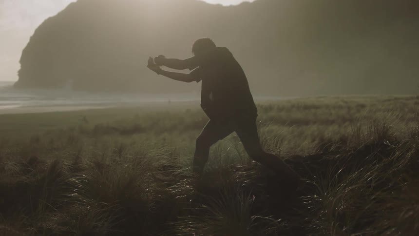 Man in a natural environment with mountains and sea dancing and gesturing his arms