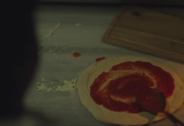 Hand holding a spoon scooping red sauce from a pot and placing it on top of white pasta