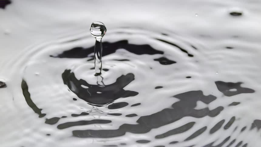 Water splash causes a water droplet in the air with the surrounding water creating a round waves