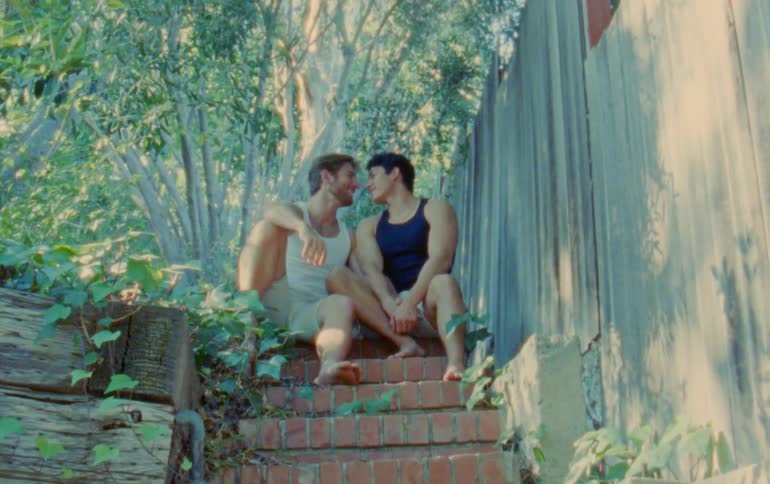 Two men sitting on a brick staircase kissing and cuddling each other