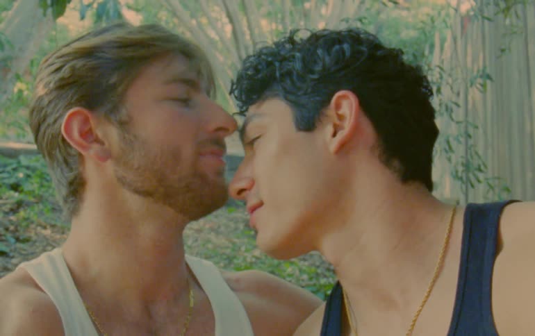 Man kisses another man on the lips and on forehead near some trees