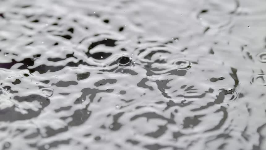 Close up of water dropping onto a body of water causing ripples on the surface