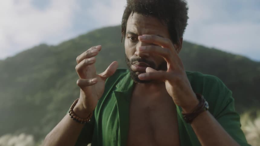 Man gazes at his hand movements while standing in front of a mountain on a cloudy day