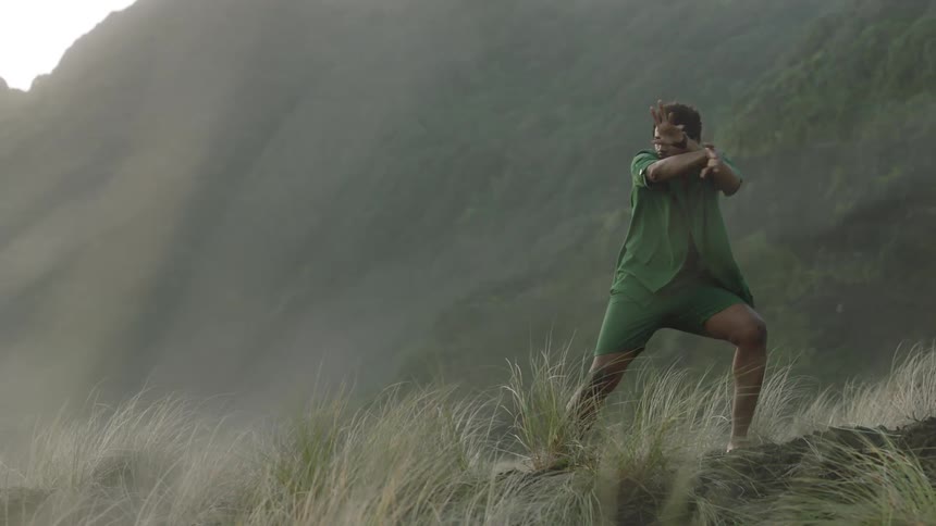 Man wearing open shirt and shorts dances near a mountain