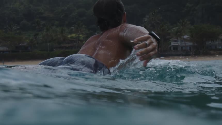 A man out at sea paddling on top of his surfboard