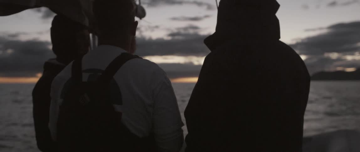 Three people stand together on a boat talking at dawn