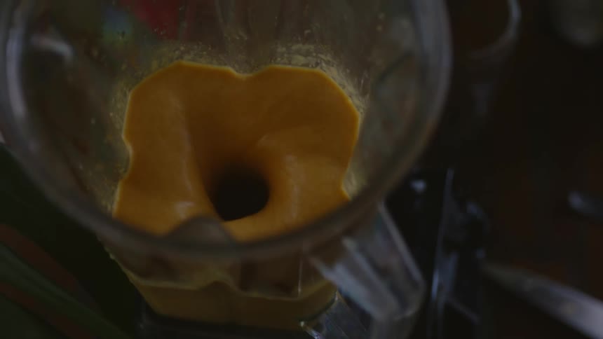 A blender with an orange liquid being mixed together on a counter in a low lit room